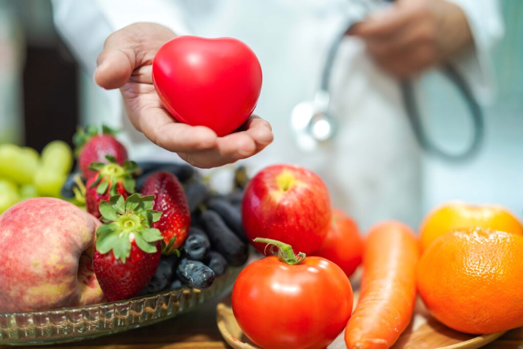 Nutritionist doctor holding orange juice with strawberry, potatoes, apples, plum, grapes, carrot, peach, pumpkin and salad vegetable on desk to instruction healthy food strong patient.